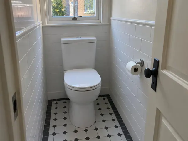 Clean white toilet in a tiled small bathroom with window in North Sydney